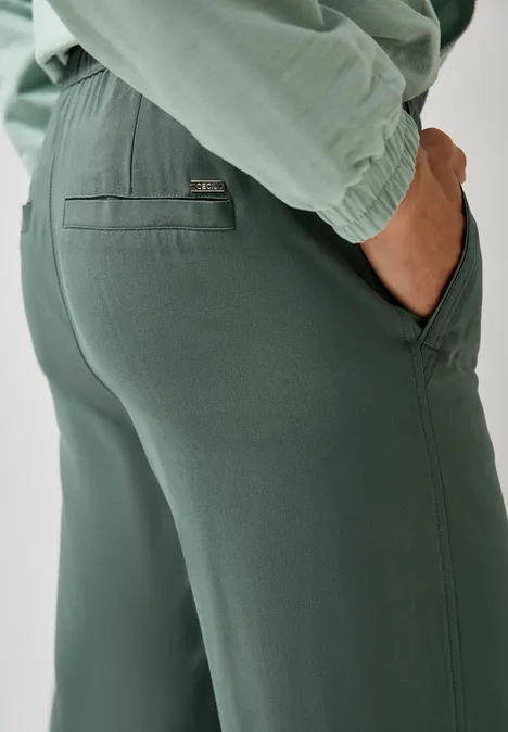 Nahaufnahme einer Person in grüner Hose, Hand in der Tasche.